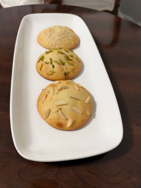Three round cookies topped with slivered almonds, pistachio and sesame on a long white platter