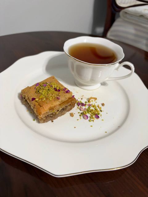 Pistachio baklava square on a white plate with a cup of tea